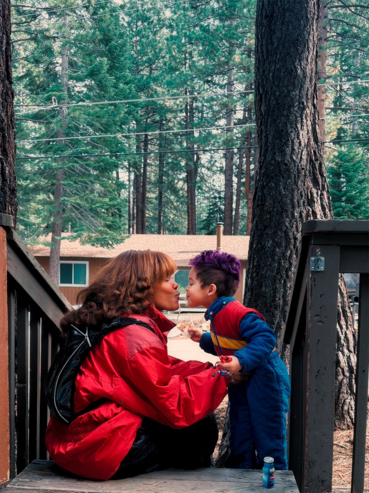Sojourn Wallace kissing her son on a wooden deck in the forest
